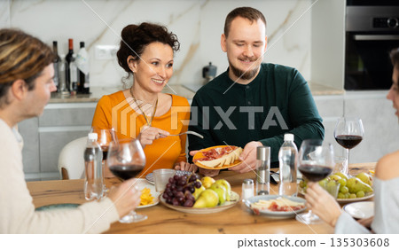 Two married couples are sitting at table, enjoying food and wine, chatting, talking, laughing. 135303608