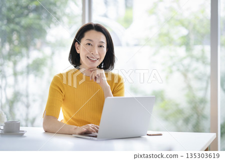 一位五十多歲的女性正在使用筆記型電腦,她面帶微笑,看著鏡頭。 一位五十多歲的女性正在使用筆記型電腦,她面帶微笑,看著鏡頭。 135303619