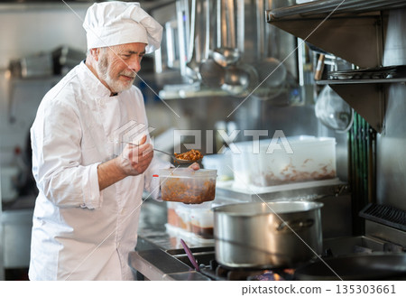 Mature man cook in kitchen is working near stove Mature man cook in kitchen is working near stove 135303661