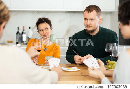 Friendly company of men and women sitting at kitchen table and enjoying the poker game. Friends play a card game at home. Evening entertainment concept 135303689