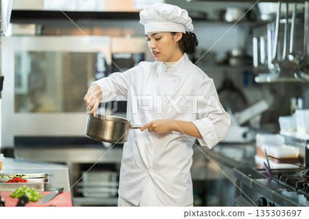 Young female cook mixing something in little saucepan 135303697