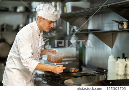 Young man cook in kitchen is working near stove 135303703