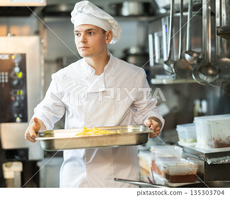 Young male cook carrying potato slices in container Young male cook carrying potato slices in container 135303704
