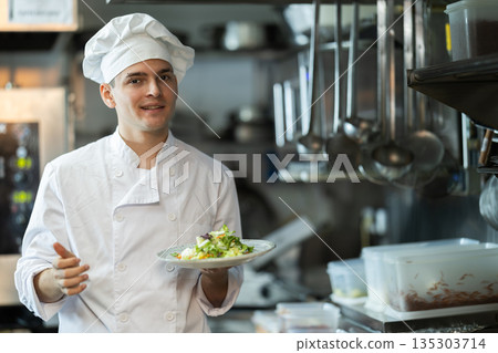 Young male chef serving fresh salad in restaurant kitchen Young male chef serving fresh salad in restaurant kitchen 135303714