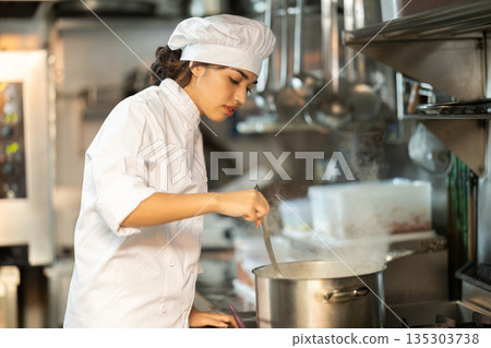 Young female chef prepares dish in saucepan Young female chef prepares dish in saucepan 135303738
