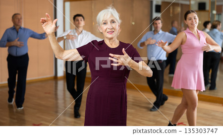 Elderly woman practicing bachata movements in dance studio Elderly woman practicing bachata movements in dance studio 135303747