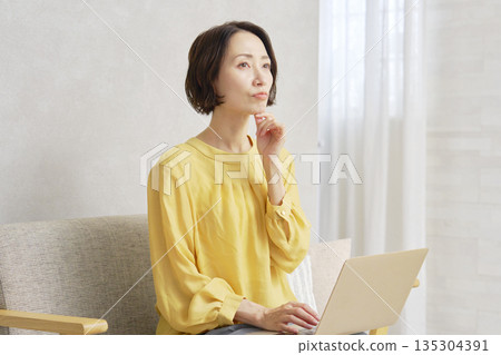 A woman using a computer in the living room thinking A woman using a computer in the living room thinking 135304391