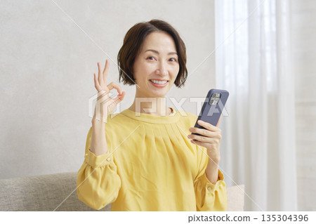 Woman using smartphone in living room OK sign 135304396