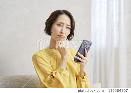 一位在客廳使用智慧型手機的女士感到擔憂 135304397