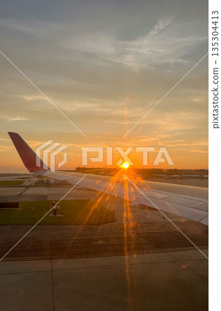 A plane wing is seen in the foreground of a sunset 135304413