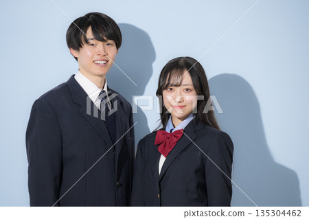 高中男生和女生並肩站在淺藍色背景前。一名女生和男生的上半身看向鏡頭。 135304462