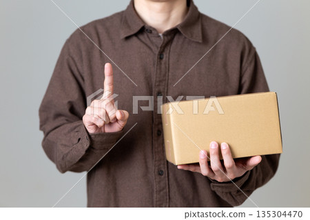 一名中年男子拿著一個紙箱,向上指著。 一名中年男子拿著一個紙箱,向上指著。 135304470
