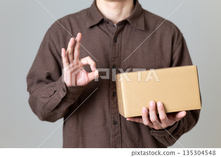 A middle-aged man holding a cardboard box and making a circle sign 135304548
