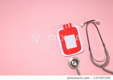 Red blood bag shape next to a gray stethoscope on pink background 135305500