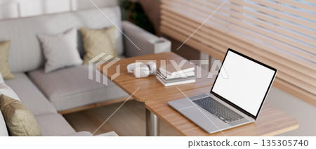 Blank screen laptop with books on wooden stool table and sofa aside blind covered glass wall in cafe Blank screen laptop with books on wooden stool table and sofa aside blind covered glass wall in cafe 135305740