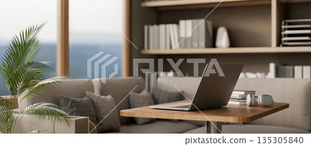 Laptop with books and headphone on wooden stool table beside fabric sofa in a living room or office. 135305840