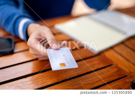 Close up of a man's hand holding or giving a credit card on wooden table in the cafe or canteen. 135305890