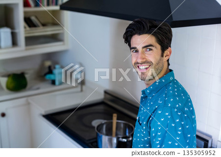 Male cooking and smiling at stovetop in home kitchen stirring pot with wooden spoon, copy space Male cooking and smiling at stovetop in home kitchen stirring pot with wooden spoon, copy space 135305952