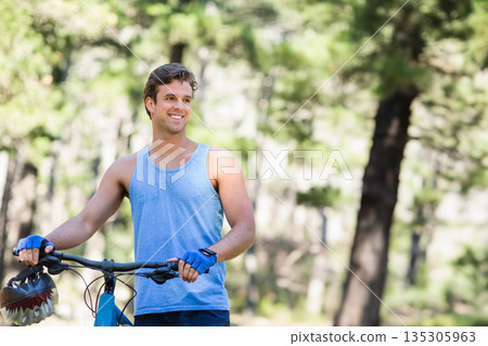 Man gripping mountain bike handlebars with gloves and helmet hanging from frame in forest clearing Man gripping mountain bike handlebars with gloves and helmet hanging from frame in forest clearing 135305963