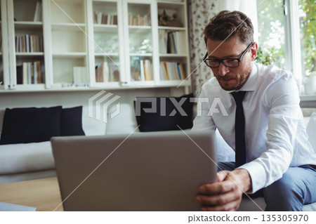 Middle-aged man in business attire adjusting laptop on table in living room, copy space 135305970
