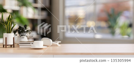Coffee cup with headphone aside books and potted plant on wooden table in bright living room or cafe 135305994