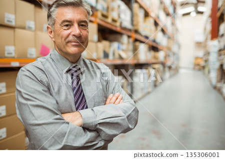 Senior man wearing shirt, tie standing with arms crossed in warehouse with racks, boxes, copy space Senior man wearing shirt, tie standing with arms crossed in warehouse with racks, boxes, copy space 135306001