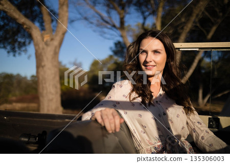 Woman leaning against off-road vehicle seat in wooded clearing in golden light, copy space 135306003