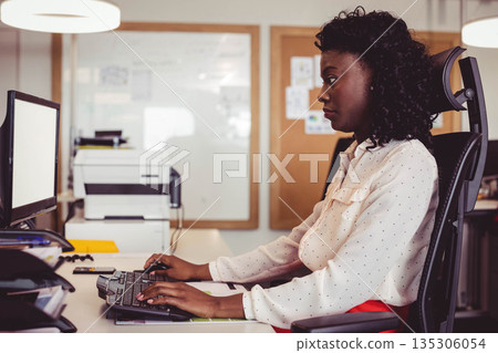 African American woman typing at office desk in office attire with keyboard, monitor, copy space African American woman typing at office desk in office attire with keyboard, monitor, copy space 135306054