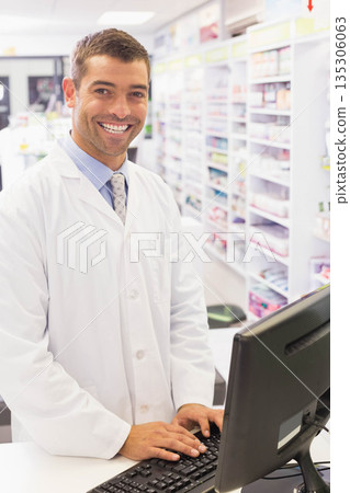 Male pharmacist in lab coat standing behind counter typing on keyboard near medication shelves Male pharmacist in lab coat standing behind counter typing on keyboard near medication shelves 135306063