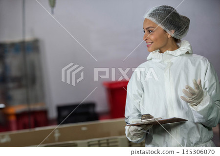 Female lab technician smiling and holding clipboard in lab wearing protective gear, copy space 135306070