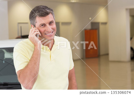 Senior man calling on smartphone inside automobile showroom next to white car and wooden partition 135306074
