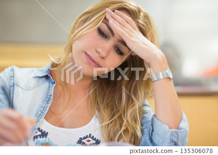 Leaning forward, female student holding pen and writing on paper at study desk wearing wristwatch 135306078