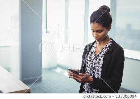 Asian and African American woman standing by window in office holding smartphone, copy space 135306094