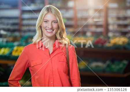Woman smiling in red-orange shirt carrying purse strap at grocery store bins of produce 135306126