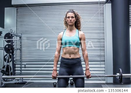 Female athlete lifting loaded barbell and performing deadlift at gym near weight rack by metal door Female athlete lifting loaded barbell and performing deadlift at gym near weight rack by metal door 135306144