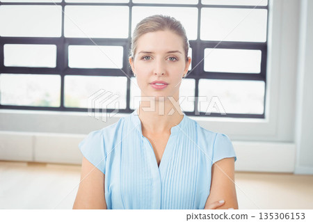 Woman wearing blue sleeveless blouse standing with arms crossed in bright studio with grid window Woman wearing blue sleeveless blouse standing with arms crossed in bright studio with grid window 135306153