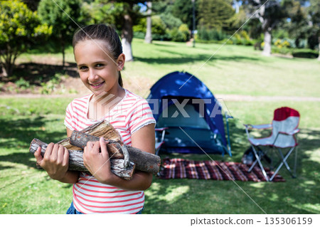 Girl carrying firewood logs standing on blanket in park near camping tent, copy space Girl carrying firewood logs standing on blanket in park near camping tent, copy space 135306159