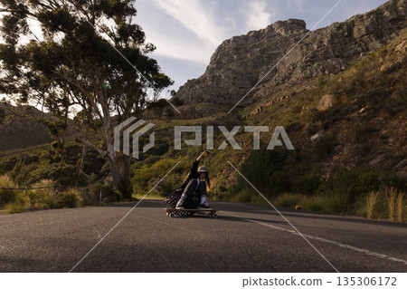 Female skateboarder crouching low on longboard under white helmet gliding down mountain road 135306172