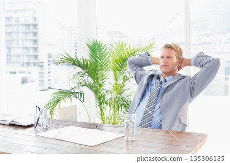 Businessman in grey suit leaning back at desk in office with notebook pen holder, copy space Businessman in grey suit leaning back at desk in office with notebook pen holder, copy space 135306185