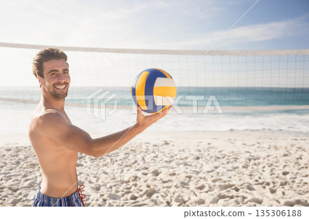 Athletic male standing on sandy beach holding volleyball near net under clear sky, copy space Athletic male standing on sandy beach holding volleyball near net under clear sky, copy space 135306188