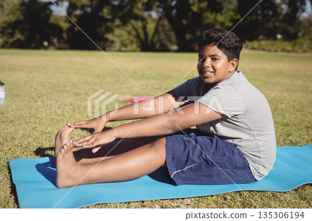 Asian child stretching forward on blue yoga mat in park with pink mat and water bottle 135306194