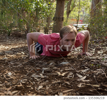 Adult male wearing red shirt doing push-up on forest floor with dry leaves, twigs Adult male wearing red shirt doing push-up on forest floor with dry leaves, twigs 135306219