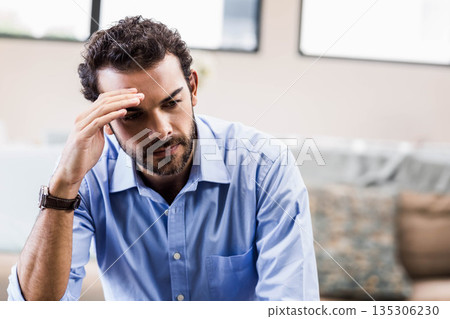 Man sitting on sofa in lounge area leaning forward pressing forehead wearing watch with cushions 135306230