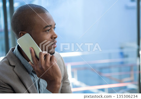 African American man in blazer holding smartphone to ear by glass railing in office, copy space 135306234
