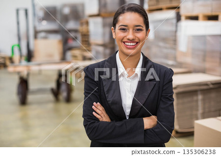 Hispanic woman standing with crossed arms and smiling in warehouse with pallet jack and boxes Hispanic woman standing with crossed arms and smiling in warehouse with pallet jack and boxes 135306238