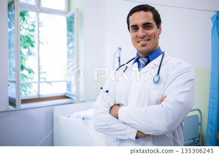 Mid-adult male doctor standing in medical exam room wearing white coat with stethoscope, copy space Mid-adult male doctor standing in medical exam room wearing white coat with stethoscope, copy space 135306245