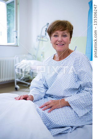 Senior woman sitting in hospital on bed holding IV line using over-bed trapeze bar wearing gown 135306247
