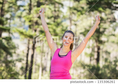 Woman in twenties stretching in sunlit forest wearing fuchsia tank top and black sports bra 135306261