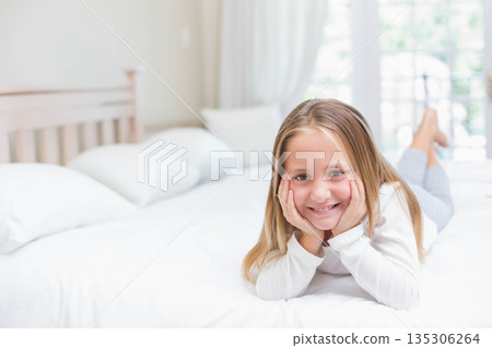 Female child smiling gently while lying on bed in bedroom under sheer curtains with white pillows Female child smiling gently while lying on bed in bedroom under sheer curtains with white pillows 135306264