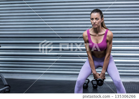 Woman in her 30s in sportswear performing wide-stance black kettlebell deadlift in gym, copy space 135306266